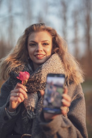 Woman holding a phone and a rose outdoors